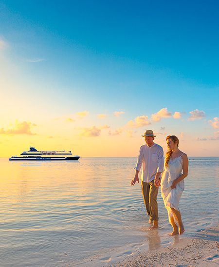 Coppia uomo e donna che passeggiano sulla battigia al tramonto. In lontananza una nave della Grimaldi Lines.