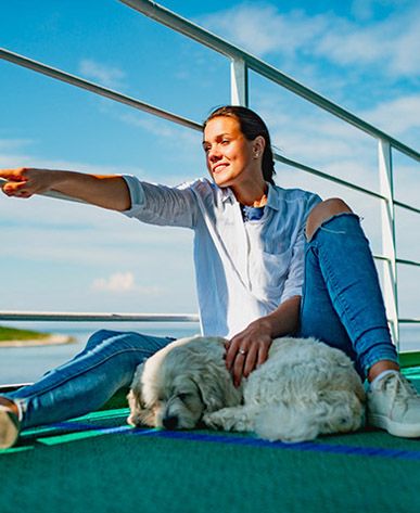 Ragazza sorridente sul ponte di una nave che accarezza un cane bianco