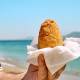 Typical Sicilian street food on seaside background. Hand of man holding hot palatable arancina (deep fried rice balls with meat) in the beach. Take out food.